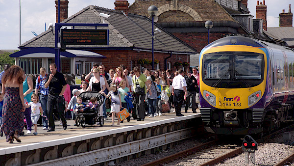 A picture of a train on the tracks with passengers alighting the train.
