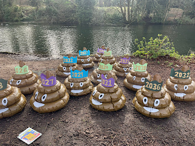 14 giant inflatable poo emojis next to a body of water. Each poo has a crown with a year written on it (to represent 14 years of illegal sewage pollution)