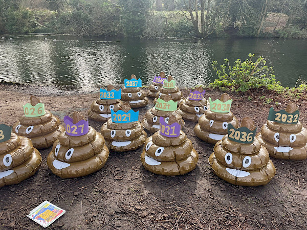 14 giant inflatable poo emojis next to a body of water. Each poo has a crown with a year written on it (to represent 14 years of illegal sewage pollution)