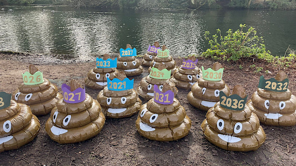 14 giant inflatable poo emojis next to a body of water. Each poo has a crown with a year written on it (to represent 14 years of illegal sewage pollution)