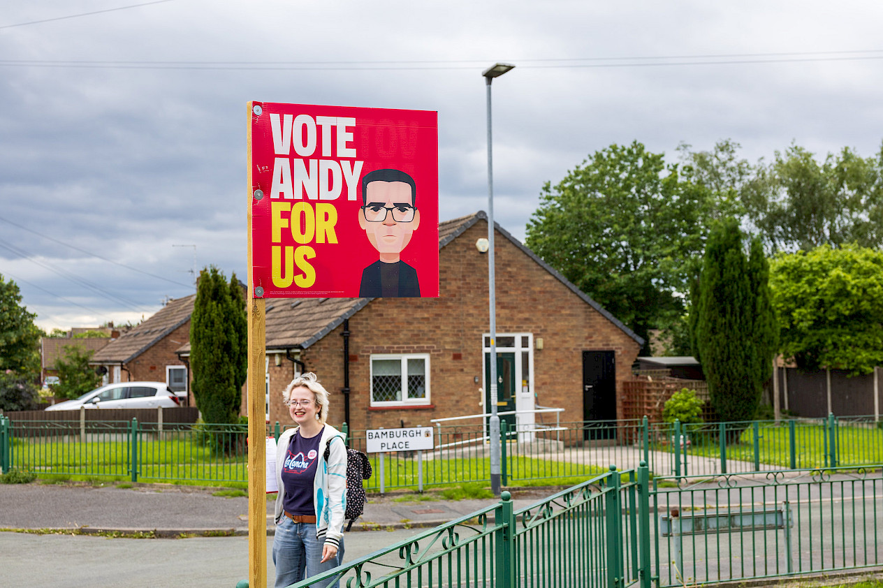 Photo: Young woman stands by a "Vote Andy for us" sign on a residential street.