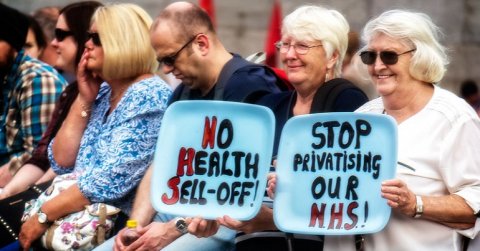 A group of protesters with signs reading "No health sell off" and "stop privatising our NHS"