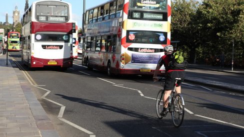 Two double decker buses driving with a cyclist behind them