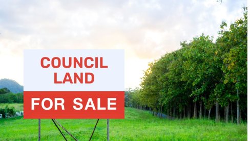 Picture of fields and woodland obscured by a large sign saying 'Council Land for Sale'