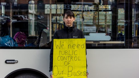 Woman holding a placard saying we need public control of our buses
