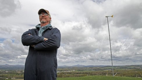 Picture of Bryan Davis standing on the hilltop with his wind turbine 